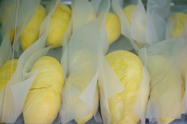 Beyaz kağıda sarılmış taze durian meyveleri, sarı rengini vurgulayan sıcak ışıklarla bir pazarda sergileniyor.