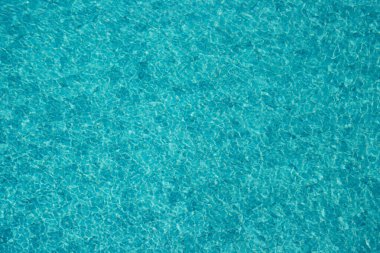 Parıldayan yansımaları ve güneş ışığı altında dalgalanmaları olan canlı mavi su yüzeyi.