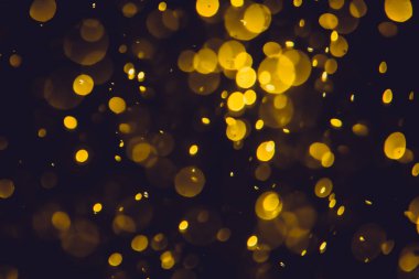 Koyu bir arka planda farklı boyut ve renklerde odanmamış altın bokeh ışıkları.