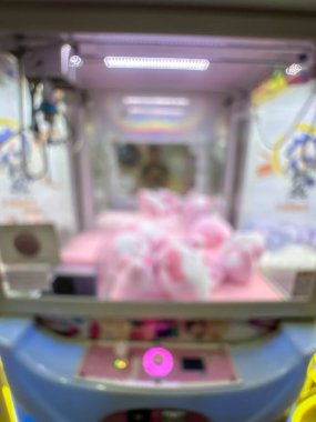 Pembe pelüş oyuncaklarla dolu renkli bir pençe makinesi oyuncuları eğlenceli bir oyun salonunda şanslarını denemeye davet ediyor..