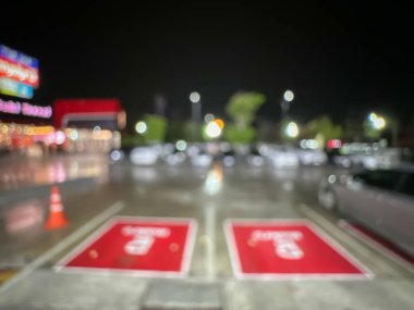 Geceleri bir marketin park alanının bulanık görüntüsü, parlak ışıklı park alanları ve aydınlatılmış mağaza tabelaları.