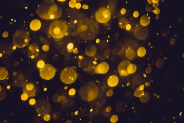 Koyu bir arka planda farklı boyut ve renklerde odanmamış altın bokeh ışıkları.