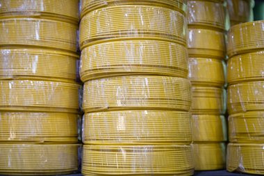 Stacks of yellow electric wire tubing coils, wrapped in protective plastic, arranged in vertical rows, captured in a warehouse setting. clipart