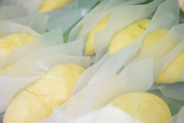 Beyaz kağıda sarılmış taze durian meyveleri, sarı rengini vurgulayan sıcak ışıklarla bir pazarda sergileniyor.