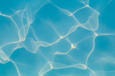 Parlak güneş ışığı yansımalarıyla canlı mavi yüzme havuzu suyunun yakın çekimi dinamik desenler oluşturur.