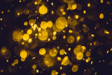 Koyu bir arka planda farklı boyut ve renklerde odanmamış altın bokeh ışıkları.