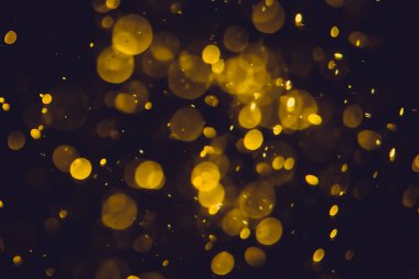 Koyu bir arka planda farklı boyut ve renklerde odanmamış altın bokeh ışıkları.