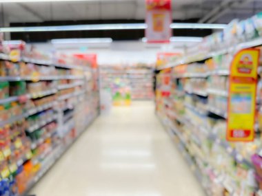 Renkli paketlenmiş ürünler ve parlak ışıklandırmalarla dolu bir süpermarket koridorunun bulanık görüntüsü.
