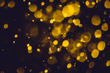 Koyu bir arka planda farklı boyut ve renklerde odanmamış altın bokeh ışıkları.