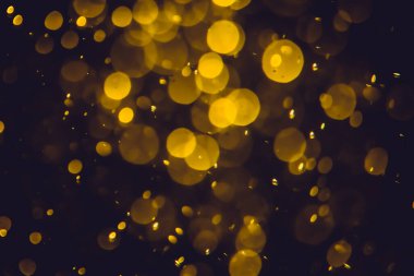 Koyu bir arka planda farklı boyut ve renklerde odanmamış altın bokeh ışıkları.