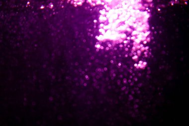 Soyut bulanık mor parıltı dokusu ışıltılı bokeh ışıklarıyla şenlikli bir zemin oluşturuyor.