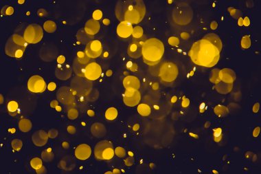 Koyu bir arka planda farklı boyut ve renklerde odanmamış altın bokeh ışıkları.