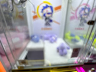 Pembe pelüş oyuncaklarla dolu renkli bir pençe makinesi oyuncuları eğlenceli bir oyun salonunda şanslarını denemeye davet ediyor..