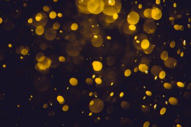Koyu bir arka planda farklı boyut ve renklerde odanmamış altın bokeh ışıkları.