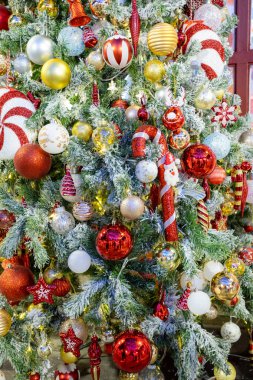 Süslü Noel ağacı, kırmızı, altın ve gümüş takılar, şeker kamışları ve süslü heykelcikler de dahil olmak üzere canlı süslemelerle süslenmiş. Donmuş dallar ve ılık peri ışıklarıyla çevrili, neşeli bir bayram ortamı yaratıyor..