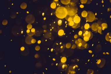 Koyu bir arka planda farklı boyut ve renklerde odanmamış altın bokeh ışıkları.