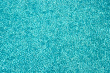 Parıldayan yansımaları ve güneş ışığı altında dalgalanmaları olan canlı mavi su yüzeyi.