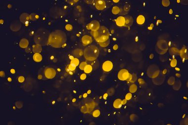 Koyu bir arka planda farklı boyut ve renklerde odanmamış altın bokeh ışıkları.