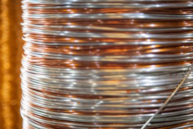 Üst üste yığılmış metalik tel bobinlerin yakın çekim görüntüleri karmaşık desenlerini ve yansıtıcı yüzeylerini gösteriyor. Görüntü, sıkıca sarılmış tellerdeki ışık ve gölgenin etkileşimini yakalıyor. Endüstriyel maddedeki ustalığı ve hassasiyeti vurguluyor.