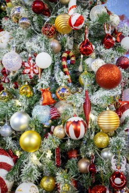 Süslü Noel ağacı, kırmızı, altın ve gümüş takılar, şeker kamışları ve süslü heykelcikler de dahil olmak üzere canlı süslemelerle süslenmiş. Donmuş dallar ve ılık peri ışıklarıyla çevrili, neşeli bir bayram ortamı yaratıyor..