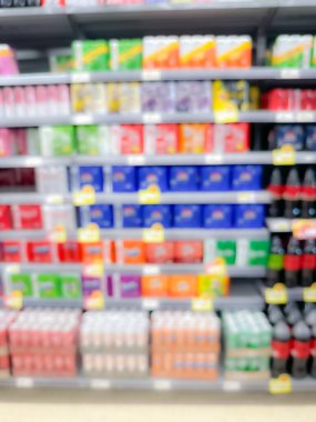 Renkli paketlenmiş ürünler ve parlak ışıklandırmalarla dolu bir süpermarket koridorunun bulanık görüntüsü.