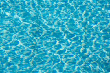 Işıldayan mavi su yüzeyine yakın çekim. Karmaşık ışık yansımaları dinamik dalgalanmalar yaratıyor. Ferahlatıcı ve yazlık bir ortam yaratıyor..