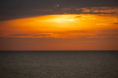 Güneş ufkun altına batıyor, sakin denizin üzerine altın bir parıltı saçıyor. Yalnız bir yelkenli körfez boyunca huzur içinde süzülürken hafif bir esinti suyu dalgalandırır. Martılar tepeden ağlar, sakin atmosferi artırır..