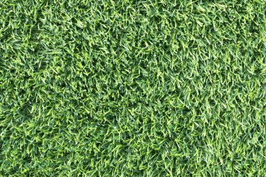 yemyeşil suni bir çimenliğe yakın çekim. Çimenlerin sentetik yaprakları mükemmel bir şekilde hizalanmış ve halı benzeri bir arka plan oluşturuyor.