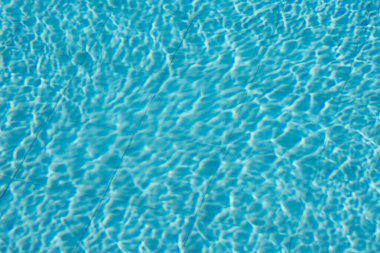 Işıldayan mavi su yüzeyine yakın çekim. Karmaşık ışık yansımaları dinamik dalgalanmalar yaratıyor. Ferahlatıcı ve yazlık bir ortam yaratıyor..