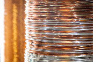 Üst üste yığılmış metalik tel bobinlerin yakın çekim görüntüleri karmaşık desenlerini ve yansıtıcı yüzeylerini gösteriyor. Görüntü, sıkıca sarılmış tellerdeki ışık ve gölgenin etkileşimini yakalıyor. Endüstriyel maddedeki ustalığı ve hassasiyeti vurguluyor.