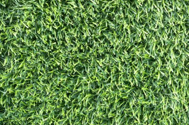 yemyeşil suni bir çimenliğe yakın çekim. Çimenlerin sentetik yaprakları mükemmel bir şekilde hizalanmış ve halı benzeri bir arka plan oluşturuyor.