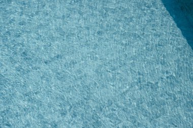 Parıldayan yansımaları ve güneş ışığı altında dalgalanmaları olan canlı mavi su yüzeyi.