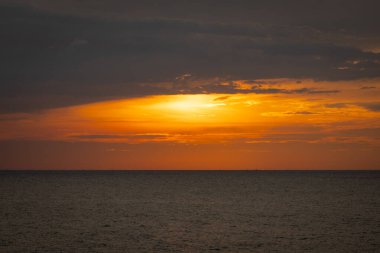 Güneş ufkun altına batıyor, sakin denizin üzerine altın bir parıltı saçıyor. Yalnız bir yelkenli körfez boyunca huzur içinde süzülürken hafif bir esinti suyu dalgalandırır. Martılar tepeden ağlar, sakin atmosferi artırır..