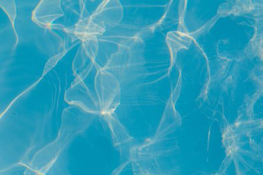 Parlak güneş ışığı yansımalarıyla canlı mavi yüzme havuzu suyunun yakın çekimi dinamik desenler oluşturur.