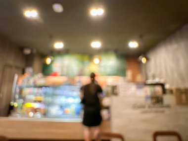 Sıcak ışıklandırmalı, rahat, bulanık bir kafe sahnesi, tezgahta bir kadın, ve bir kutu yiyecek.