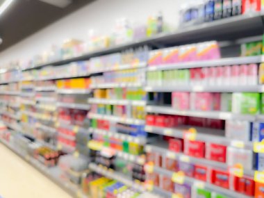 Renkli paketlenmiş ürünler ve parlak ışıklandırmalarla dolu bir süpermarket koridorunun bulanık görüntüsü.