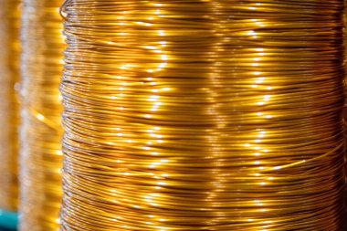 Üretim ortamında düzgün bir şekilde yaralanmış bakır tel bobinlerin yakın çekim görüntüsü. Görüntü, bakır parlak metalik parıltısını bulanık endüstriyel arka plana vurguluyor ve maddenin elektrik ve endüstriyel alandaki önemini vurguluyor. 