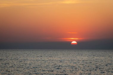 Sakin bir günbatımı sahnesi ufkun altında yavaşça kayboluyor, sakin okyanusun üzerine yumuşak, pembe ve turuncu renkler döküyor..