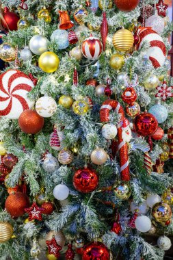 Süslü Noel ağacı, kırmızı, altın ve gümüş takılar, şeker kamışları ve süslü heykelcikler de dahil olmak üzere canlı süslemelerle süslenmiş. Donmuş dallar ve ılık peri ışıklarıyla çevrili, neşeli bir bayram ortamı yaratıyor..