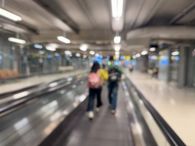 Havaalanı terminali boyunca yürüyen bir yürüyüş yolu ve modern mimari detaylarla yürüyen gezginlerin bulanık görüntüsü.