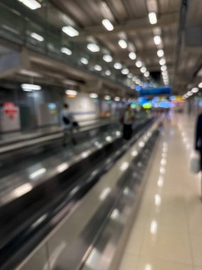 Havaalanı terminali boyunca yürüyen bir yürüyüş yolu ve modern mimari detaylarla yürüyen gezginlerin bulanık görüntüsü.