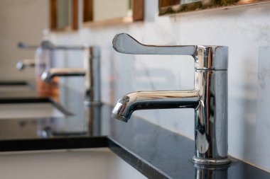 Pürüzsüz krom musluk cilalanmış siyah mermer tezgahın üzerine kurulmuş, arka planda bulanık beyaz mermer arkaplanı var.