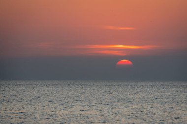 Sakin bir günbatımı sahnesi ufkun altında yavaşça kayboluyor, sakin okyanusun üzerine yumuşak, pembe ve turuncu renkler döküyor..
