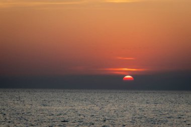 Sakin bir günbatımı sahnesi ufkun altında yavaşça kayboluyor, sakin okyanusun üzerine yumuşak, pembe ve turuncu renkler döküyor..