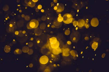 Koyu bir arka planda farklı boyut ve renklerde odanmamış altın bokeh ışıkları.