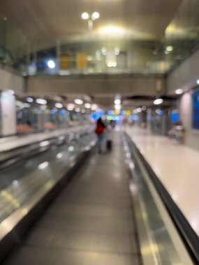 Havaalanı terminali boyunca yürüyen bir yürüyüş yolu ve modern mimari detaylarla yürüyen gezginlerin bulanık görüntüsü.