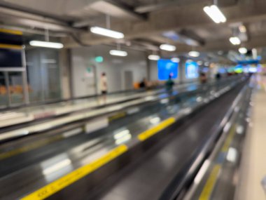 Havaalanı terminali boyunca yürüyen bir yürüyüş yolu ve modern mimari detaylarla yürüyen gezginlerin bulanık görüntüsü.