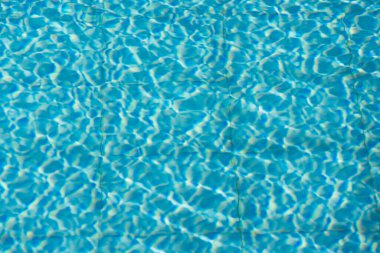 Işıldayan mavi su yüzeyine yakın çekim. Karmaşık ışık yansımaları dinamik dalgalanmalar yaratıyor. Ferahlatıcı ve yazlık bir ortam yaratıyor..