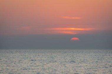 Sakin bir günbatımı sahnesi ufkun altında yavaşça kayboluyor, sakin okyanusun üzerine yumuşak, pembe ve turuncu renkler döküyor..