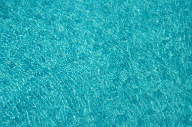 Parıldayan yansımaları ve güneş ışığı altında dalgalanmaları olan canlı mavi su yüzeyi.